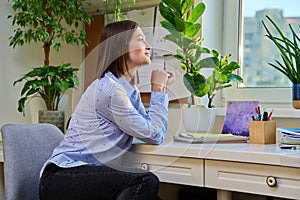Young smiling woman looking out the window at home, sitting at desk