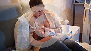 Young smiling woman lying in bed feeding her newborn baby boy with breast milk in dark bedroom Concept of healthy and