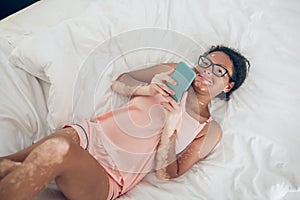 Young smiling woman lying in bed and texting