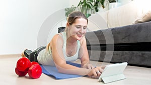 Young smiling woman lying on floor and watching trainin videos on tablet