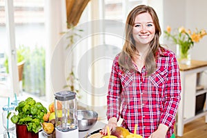 Young smiling woman making smoothie with fresh greens in the blender in kitchen at home