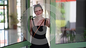 Young smiling woman opens a glass door