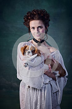 Young smiling woman with pale skin and blushing cheeks holding little dog king charles terrier  over dark green