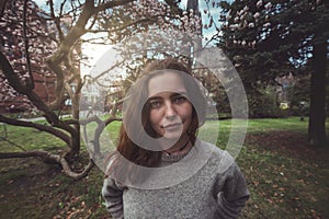 Young, smiling woman in a park in front of a magnolia tree