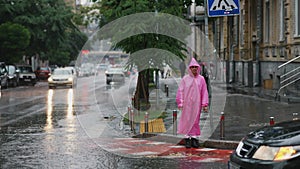 Young smiling woman with a pink raincoat crosses the road on a rainy day.