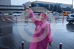 Young smiling woman in a pink raincoat enjoying a rainy day.