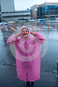 Young smiling woman in a pink raincoat enjoying a rainy day.