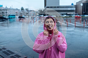 Young smiling woman in a pink raincoat enjoying a rainy day.