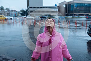 Young smiling woman in a pink raincoat enjoying a rainy day.