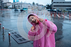 Young smiling woman in a pink raincoat enjoying a rainy day.