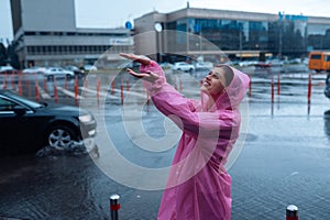 Young smiling woman in a pink raincoat enjoying a rainy day.