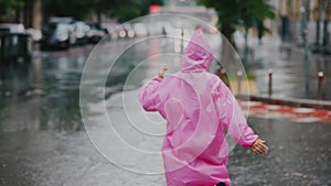 Young smiling woman with a pink raincoat while enjoying a walk through the city on a rainy day.