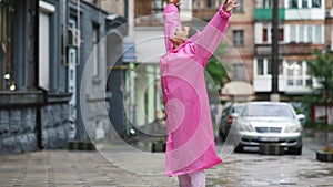 Young smiling woman with a pink raincoat on the street while enjoying a rainy day.