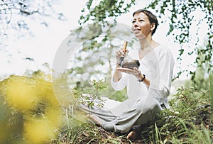 Young smiling woman playing on brass Tibetan singing bowl outdoor. Sound therapy and meditation