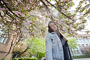 Young smiling woman posing on the background of blooming sakura
