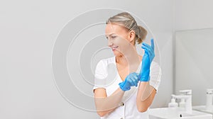 A young smiling woman puts on medical gloves. The cosmetologist is preparing for the procedure. Copy space. Professional