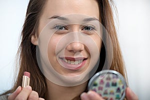 Young and smiling woman putting lipstick