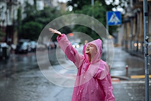 Young smiling woman with raincoat while enjoying a rainy day.