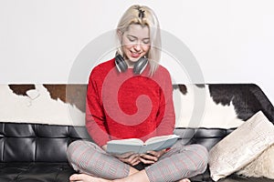 Young smiling woman reading a book on a couch in living room