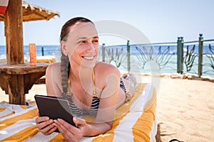 Young smiling woman reading book lounging at the beach