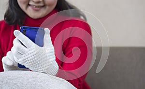 Young smiling woman in red sweater using modern smartphone to video call on sofa in living room