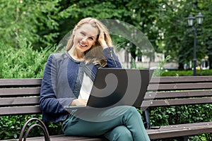 young smiling woman relaxing on the bench in the city park with laptop