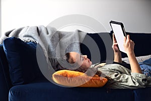 Young Smiling Woman Relaxing At Home Lying On Sofa Reading Book On Digital Tablet
