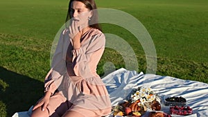 Young smiling woman relaxing outdoors and having a picnic on a blanket on grass