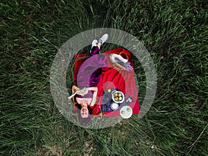 Young smiling woman relaxing outdoors and having a picnic, she is lying down on a blanket on the grass, top view.