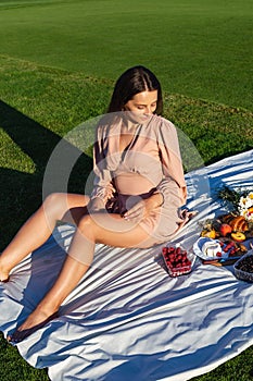 Young smiling woman relaxing outdoors and having a picnic, she is sitting on a blanket on the grass