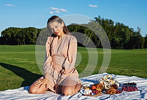 Young smiling woman relaxing outdoors and having a picnic, she is sitting on a blanket on the grass