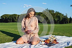 Young smiling woman relaxing outdoors and having a picnic, she is sitting on a blanket on the grass