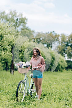 young smiling woman with retro bicycle with wicker basket full of flowers photo