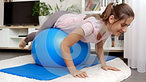 Young smiling woman rolling and balancing on big blue ball while doing sports and yoga at home