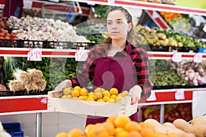 Young smiling woman salesman carrying box with yellow plums