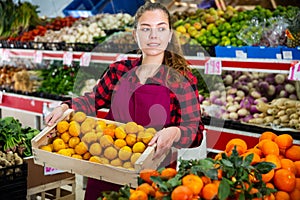 Young smiling woman salesman carrying box with yellow plums