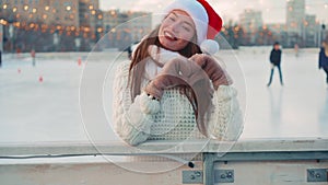 Young smiling woman Santa hat ice skating outside on ice rink dressed white sweater. Christmas holiday, active winter