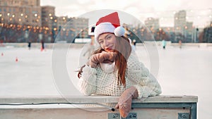 Young smiling woman Santa hat ice skating outside on ice rink dressed white sweater. Christmas holiday, active winter