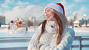 Young smiling woman Santa hat ice skating outside on ice rink dressed white sweater. Christmas holiday, active winter