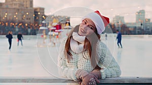 Young smiling woman Santa hat ice skating outside on ice rink dressed white sweater. Christmas holiday, active winter