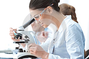 Young smiling woman scientist working with microscope