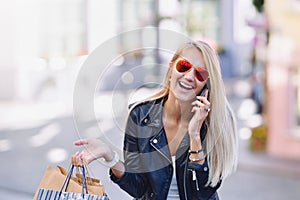 Young smiling woman with shopping bags talk by cellular telephone.