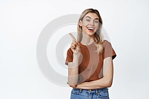 Young smiling woman showing one finger, pointing at upper left corner with happy, satisifed face, demonstrating