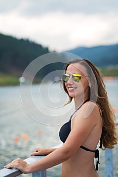 Young smiling woman in swimwear enjoying the view of a lake in the mountains