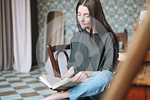 Young smiling woman teenager girl student with dark long hair in casual reading book at the home