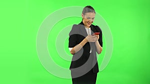 Young smiling woman texting on her phone and rejoice. Green screen