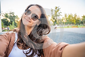 Young smiling woman in trendy summer clothes. Happy model posing in the street at sunny day. Makes pov selfie in