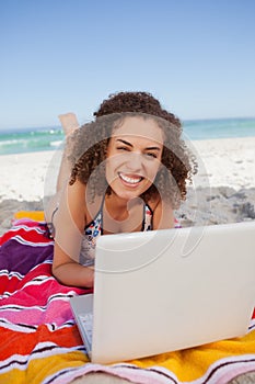 Young smiling woman typing on her laptop while lying on the beach