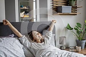 Young smiling woman waking up lying in bed stretching with pleasure. Healthy and comfortable sleep concept