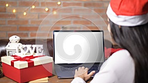 Young smiling woman wearing red Santa Claus hat making video call on social network with family and friends on Christmas day.